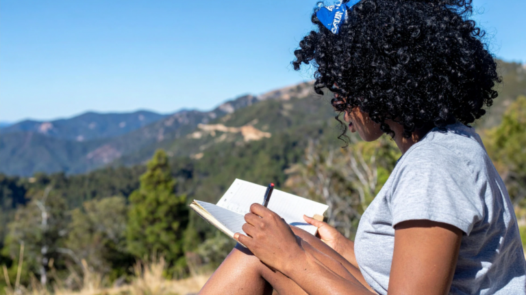 Woman sitting outdoors writing in a journal.