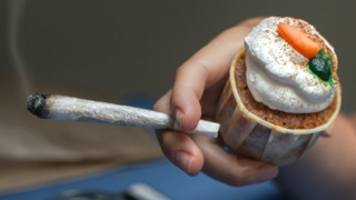Hand holding a cannabis preroll and a cupcake.