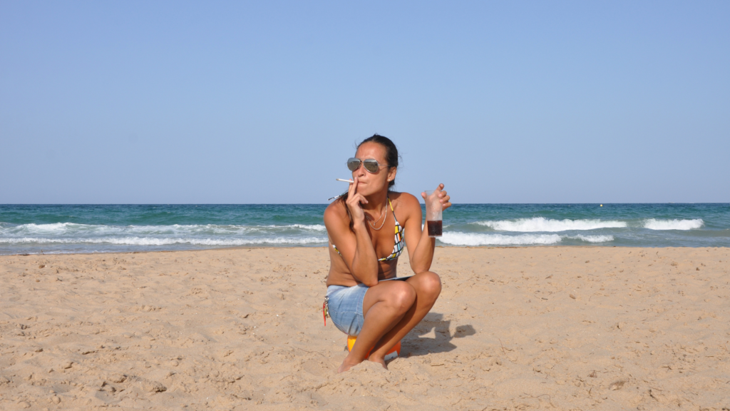 Woman smoking a pre-roll while sitting in the sand on the beach in New Jersey.